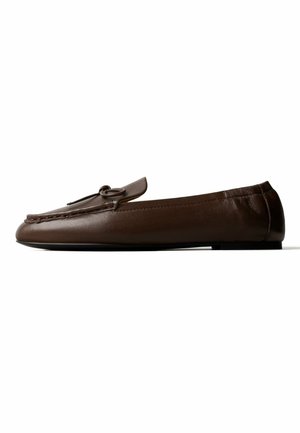 Mocassin en cuir marron avec un petit talon, coutures mocassin, et un détail de noeud décoratif sur le dessus.