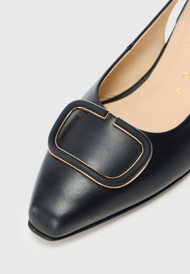 Czarna skórzana półbut z ostrym noskiem, z dużą geometryczną klamrą z czarnego materiału z akcentami w złocie na przodzie. Gładka faktura.