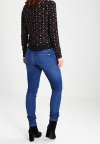 Maglione a maglia nero con motivo floreale, maniche lunghe, abbinato a jeans skinny blu e stivali neri alla caviglia. Vista posteriore.