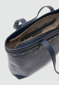 Borsetta tote in pelle blu con zip in tono oro, esterno testurizzato e dettagli in borchie. L'interno presenta una fodera a motivo e diversi scomparti.