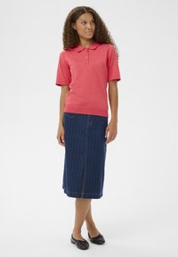 Polo rouge à manches courtes, assorti à une jupe en denim bleu foncé à rayures verticales, arrivant au genou et avec une fente à l'avant.