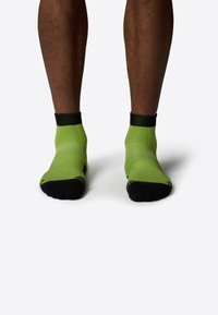 Calcetines deportivos verdes con acabado texturizado, detalles en negro en el talón y la puntera, con un diseño de longitud por la mitad de la pantorrilla.