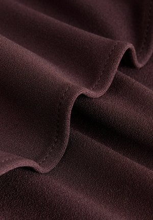 Dunkelburgunderfarbenes Gewebe mit einer weichen, glatten Textur, das subtile Wellen und gesteppte Kanten aufweist. Die Oberfläche wirkt reichhaltig und leicht strukturiert.