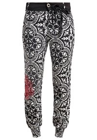 Pantalon à motifs noir et blanc avec poignets élastiques, taille à boutons, ceinture noire à nouer et détail brodé rouge sur la jambe gauche.