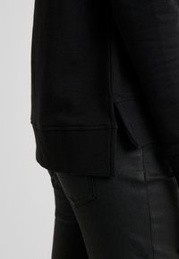 Černá mikina s žebrovaným lemem a manžetami, vyrobená z měkkého materiálu. Doplněná černými štíhlými kalhotami s jemným leskem.