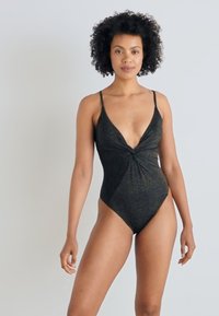 Μαύρο ολόσωμο μαγιό με βαθύ V-ντεκολτέ, κόμπο στα μπροστινά του μέρη και λεπτές τιράντες. Η λαμπερή υφή προσθέτει οπτικό ενδιαφέρον.