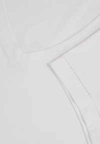 Nahaufnahme des weißen V-Ausschnitt-Shirt-Kragens und des hochgekrempelten Ärmels mit sichtbaren Nahtdetails auf glattem Stoff.
