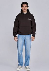 Svart luvtröja med framficka och broderad logotyp, kombinerad med ljusblå jeans med raka ben och neutralt färgade sneakers.