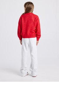 Roter Pullover mit strukturierter Oberfläche, gerippten Bündchen und Saum, kombiniert mit locker sitzenden hellgrauen Jogginghosen. Minimalistisches, lässiges Design.
