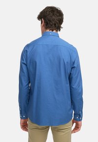 Camisa de manga larga azul de tela ligera, con cuello y puños abotonados, textura suave y un corte ligeramente relajado.