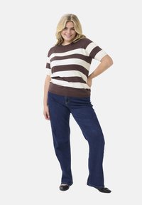 Braun- und cremefarben gestreifter kurzärmeliger Pullover, kombiniert mit dunkelblauen Schlagjeans und schwarzen Ballerinas. Gerader Saum, lässige Passform.