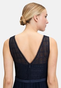 Navy sukienka z koronkowym tyłem, dekoltem w serek, ozdobnymi guzikami oraz paskiem w talii. Miękka tkanina o luźnej strukturze i zapięcie na zamek. 