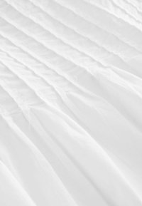 Tissu blanc avec des plis verticaux, présentant une texture lisse et une apparence légère, créant des lignes douces et fluides sur toute la surface.