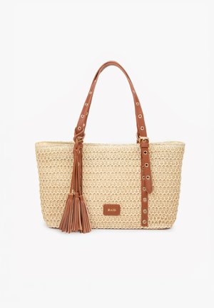 Woven beige tote bag with brown leather handles featuring eyelet details, tassel accents, and a small "RAID" label on the front.