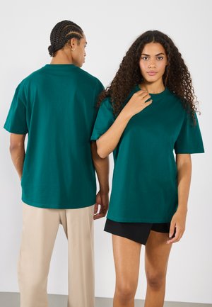 T-shirt in cotone verde, vestibilità morbida, maniche corte, colletto rotondo. Un modello di fronte, l'altro visto da dietro. Design semplice.
