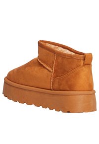 Botín de tobillo de ante marrón claro con un perfil bajo, forro suave, panel lateral elástico y una suela de goma gruesa y texturizada con un patrón.