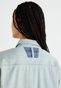 Camicia di jeans a righe con un motivo azzurro chiaro e bianco, caratterizzata da un paesaggio azzurro scuro sul retro e un colletto button-down.