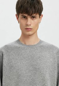 Grå strikkegenser med rund hals, myk tekstur og lange ermer; båret av en person med kort hår og store øredobber.