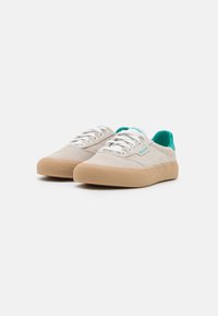Beige suede sneakers with a textured light brown rubber sole, white laces, and teal accents on the tongue and branding.