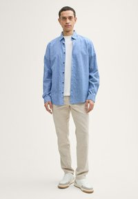 Lichtblauw, knop-up shirt met lange mouwen, gecombineerd met een wit t-shirt, beige broeken en witte sneakers met bruine accenten.