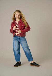 Rdeča faux usnjena jakna s ovratnikom, z zadrgo spredaj in dvema žepoma na prsih. Oblečena z majico s črtami in ohlapnimi modrimi jeansom, v kombinaciji s črnimi čevlji.