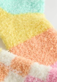 Bunt gemusterte, flauschige Socken mit weicher Textur in hellblau, gelb, pfirsich, weiß und rosa. Dickes, plüschiges Material sorgt für Wärme.