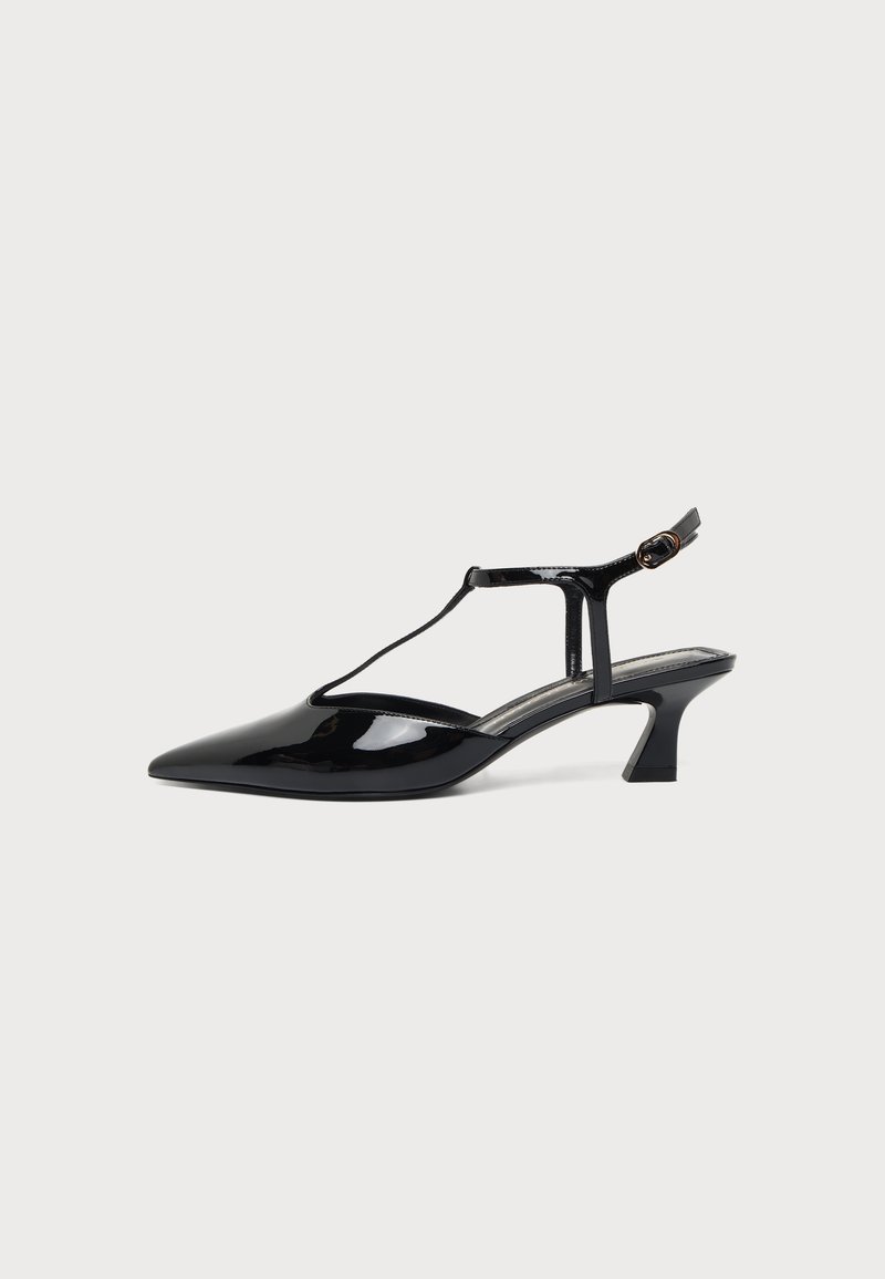 Μαύρο παπούτσι slingback από λουστρίνι με μυτερή μύτη, T-στραπ και χαμηλό κεκλιμένο τακούνι, σε λευκό φόντο.