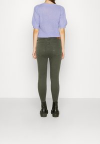 Lichtpaarse gebreide trui met korte pofmouwen, gecombineerd met olijfgroene skinny jeans en zwarte enkellaarzen. Achteraanzicht getoond.