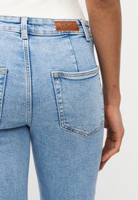 Κοντινό πλάνο ενός ατόμου που φοράει ανοιχτό μπλε τζιν με πίσω τσέπες και καφέ δερμάτινη ετικέτα μάρκας πάνω από την δεξιά τσέπη.