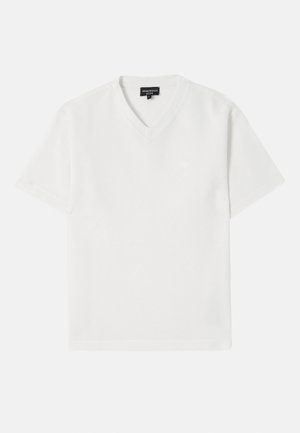 Camiseta blanca de manga corta con cuello en V, confeccionada en una tela texturizada con un patrón sutil. Presenta un pequeño logo en el pecho.