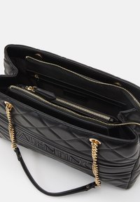 Black quilted leather handbag with gold chain straps, embossed logo, and multiple zippered interior compartments.
