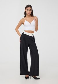 Pantaloni neri a gamba larga con vita bianca, dotati di due bottoni e una texture liscia. Abbinati a un top aderente bianco a coste.