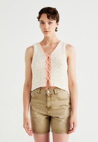 Gehaakte cropped top in crème met een perzikkleurige scalloped halslijn en gevlochten voor-detail. Gecombineerd met khaki denim shorts. Zachte textuur.