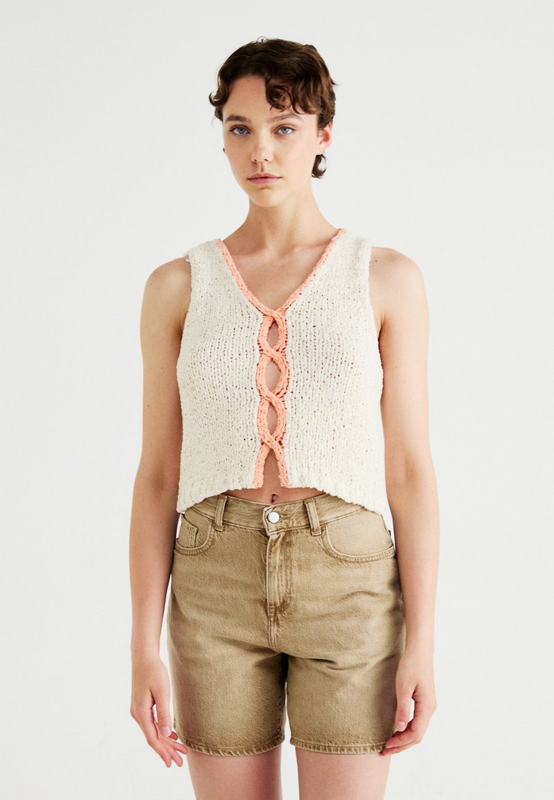 Gehaakte cropped top in crème met een perzikkleurige scalloped halslijn en gevlochten voor-detail. Gecombineerd met khaki denim shorts. Zachte textuur.