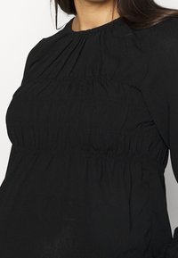 Černá dlouhá rukávová blůza se skládáním na výstřihu a v pase, vyrobená z lehkého, strukturovaného materiálu.