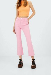 Rosafarbene Schlagjeans aus Denim mit rohem Saum. Kombiniert mit einem orangefarbenen, gerippten Croptop und schwarzen Plateausandalen.
