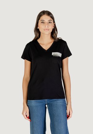 T-shirt nera a collo a V con maniche corte, caratterizzata da una piccola tasca con un design grafico. Tessuto morbido con vestibilità rilassata. Jeans in denim visibili.