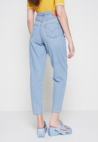 Jeans de tiro alto en azul claro con pernera recta, que cuentan con dos bolsillos traseros y una etiqueta de cuero marrón. Combinados con sandalias de plataforma azules.