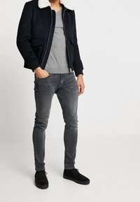 Černá bomber bunda s bílým umělým kožíškem, šedé tričko, slim-fit šedé džíny a černé semišové tenisky.