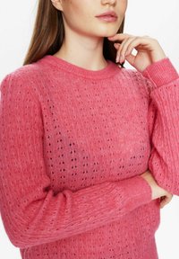 Maglione lavorato a maglia di un vivace colore rosa, con un motivo testurizzato, dotato di un collo a girocollo a coste e maniche lunghe con polsini a coste.