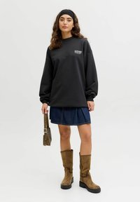 Černá oversized mikina s logem, džínová sukně, hnědé semišové kozačky až po kolena a hnědá kabelka. Hladký materiál a uvolněný střih po celou dobu.