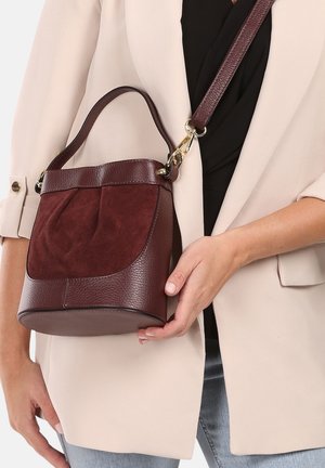 Bordeauxfarbene Handtasche mit einem strukturierten Lederkörper und einer weichen Wildlederfront. Verfügt über einen Griff und einen verstellbaren Gurt und zeigt eine runde Form.