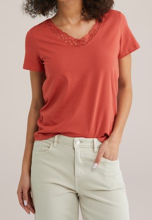 Koralfarvet bomulds-T-shirt med V-udskæring og blonderkant, kombineret med lyse beige jeans. Korte ærmer og afslappet pasform med en glat tekstur.