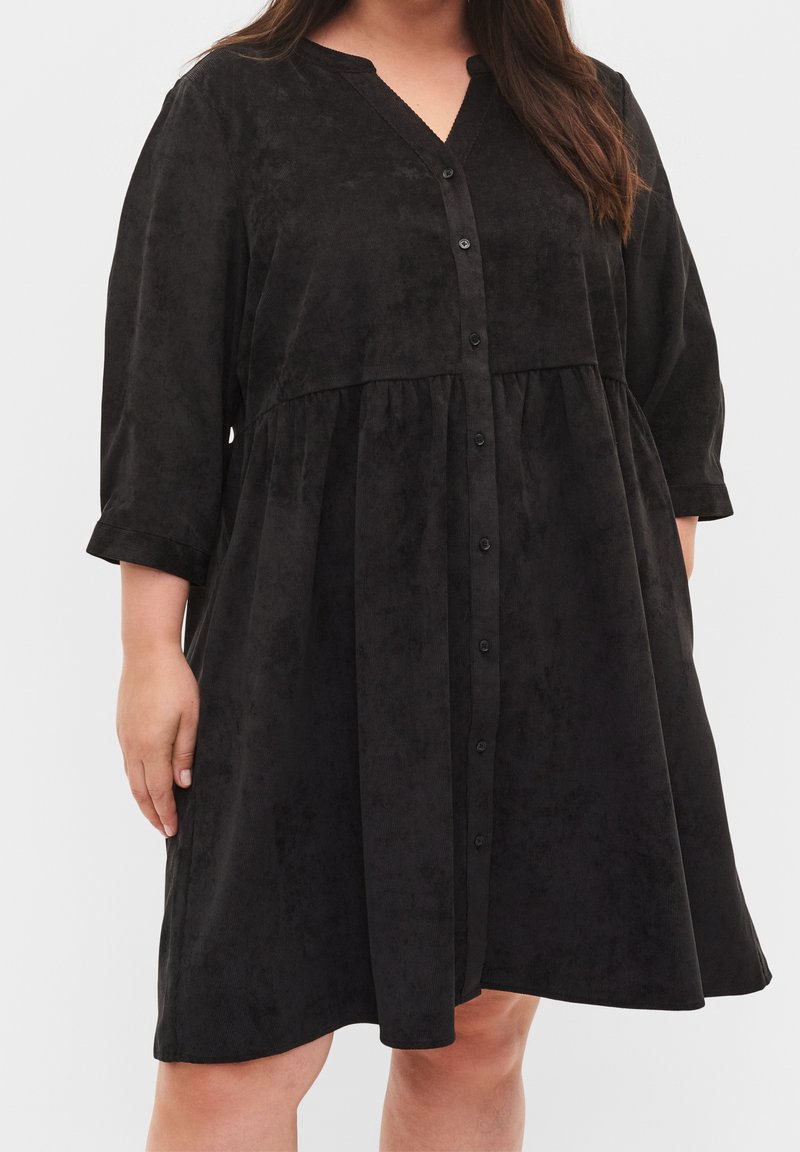 Robe noire, à boutons, avec un décolleté en V, des manches trois-quarts et une jupe évasée. Fabriquée en tissu doux et texturé.