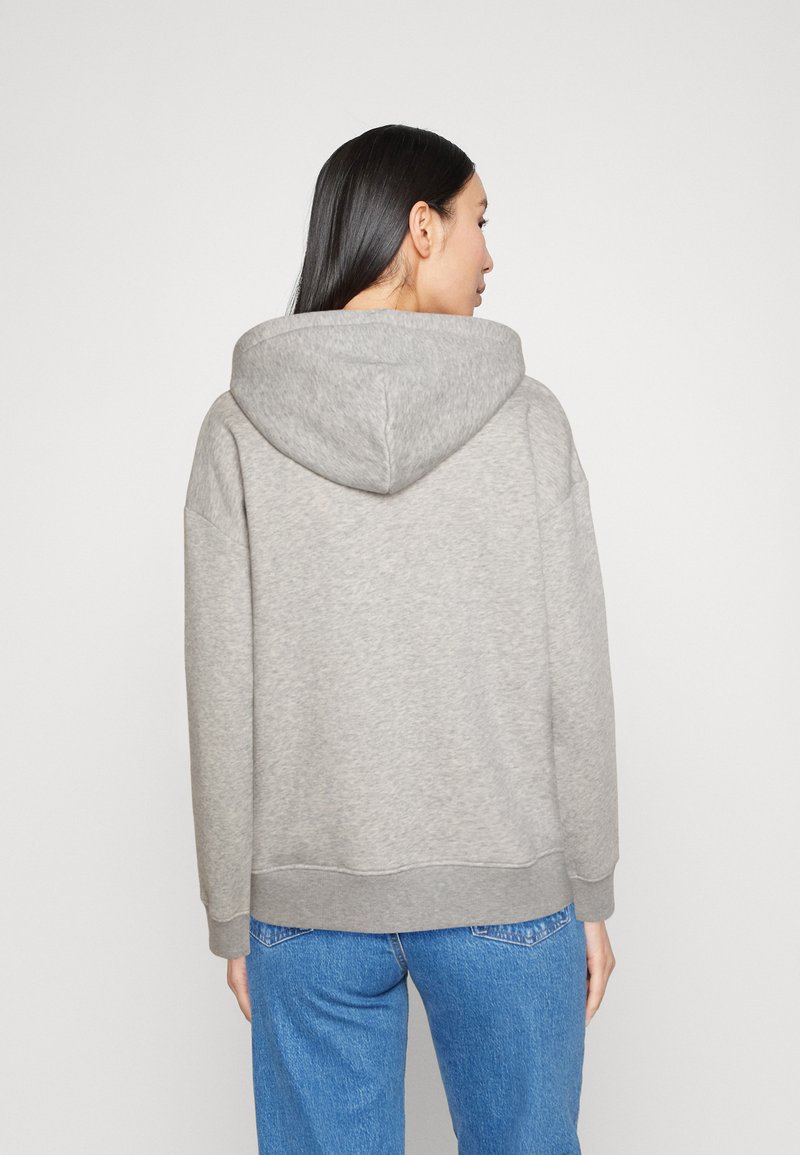 Sweat-shirt à capuche gris avec une coupe décontractée, des épaules tombantes et des poignets côtelés. Tissu chaud avec une texture douce. Porté avec un jean en denim bleu.