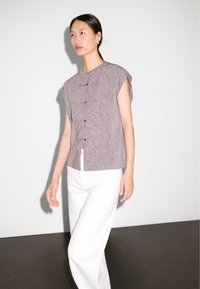 Kurzärmlige, knöpfbare Bluse aus strukturiertem Mauve-Stoff mit Stehkragen, kombiniert mit weißen, weit geschnittenen Hosen. Sauberes, minimalistisches Design.