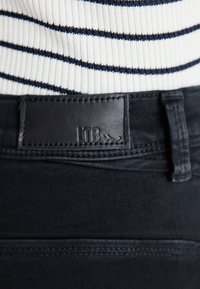 Vaqueros de mezclilla negros con una etiqueta de cuero LTB en la cintura, combinados con un top blanco de canalé con rayas marinas.