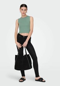 Jasnozielony prążkowany crop top, czarne wąskie dżinsy, czarna zamszowa torba na ramię z uchwytami oraz czarne klapki, stojące na jednolitym tle.