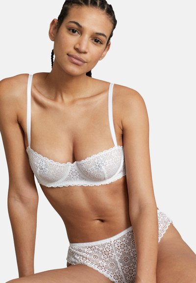 Vitt spets-lingerieset bestående av en balconette-bh med tunna remmar och dekorativa vågiga kanter, parat med matchande högmidjade trosor.