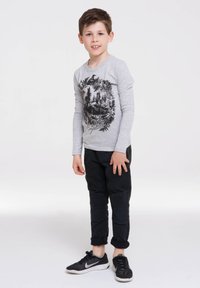 Gray long-sleeve shirt featuring a black graphic design, paired with black slim-fit pants with ribbed accents and black athletic shoes.